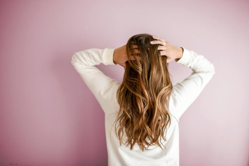 A woman with long hair standing in front of a pink wall.