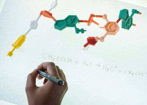  A person writing on a white board with a marker near a molecular structure.