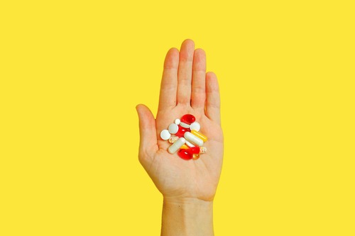 Hand holding assorted pills and capsules.