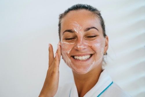 A woman smiles brightly as she applies a facial mask