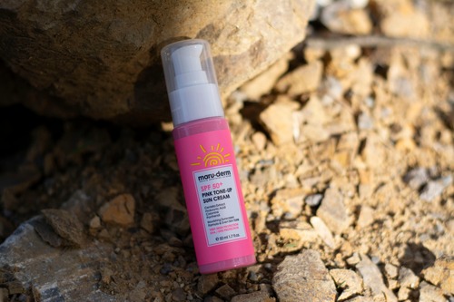 A bottle of pink sunscreen positioned atop a rugged arrangement of rocks