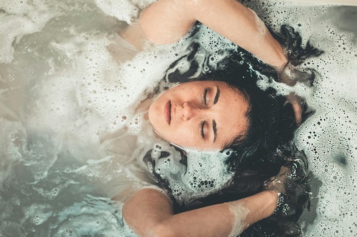 A woman relaxes in water filled with foam